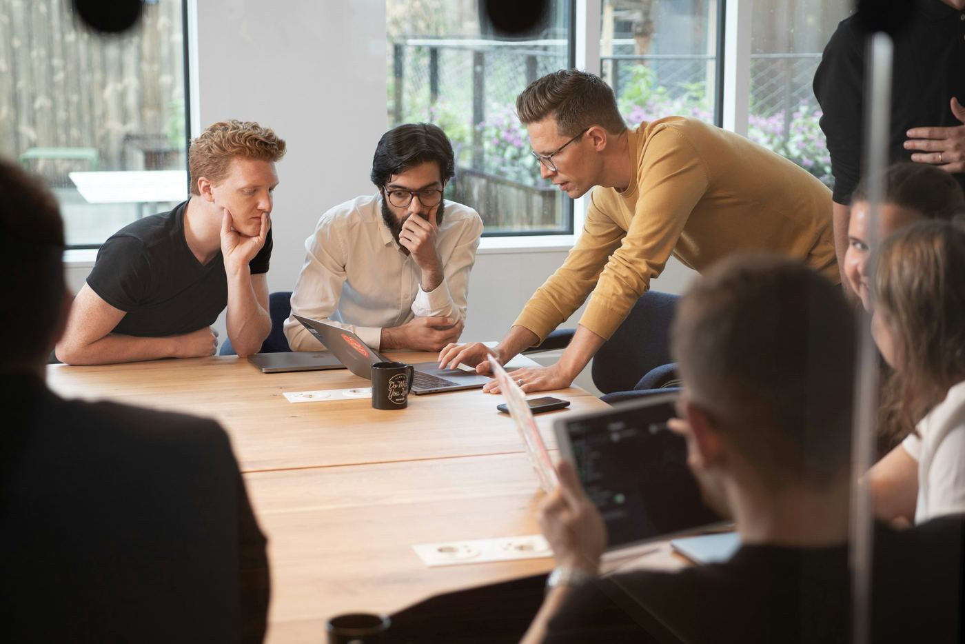 Grupo de personas reunidas alrededor de una mesa de madera revisando una laptop