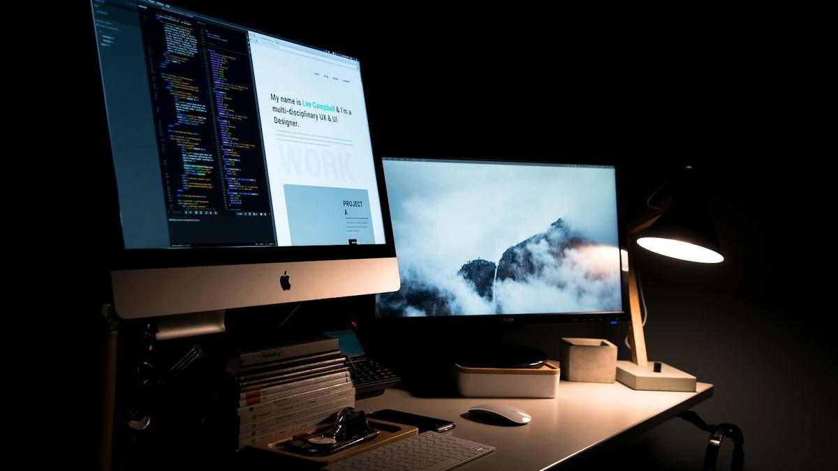 Escritorio de un desarrollador web con dos pantallas mostrando código y el diseño de un sitio