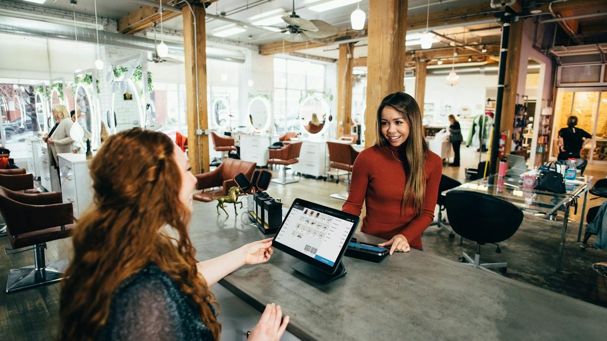 Recepción de un negocio local atendiendo a una clienta frente a una laptop
