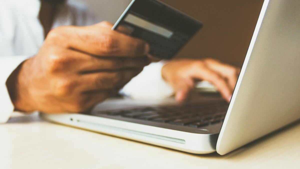 Persona pagando en línea con tarjeta de crédito frente a una computadora portátil